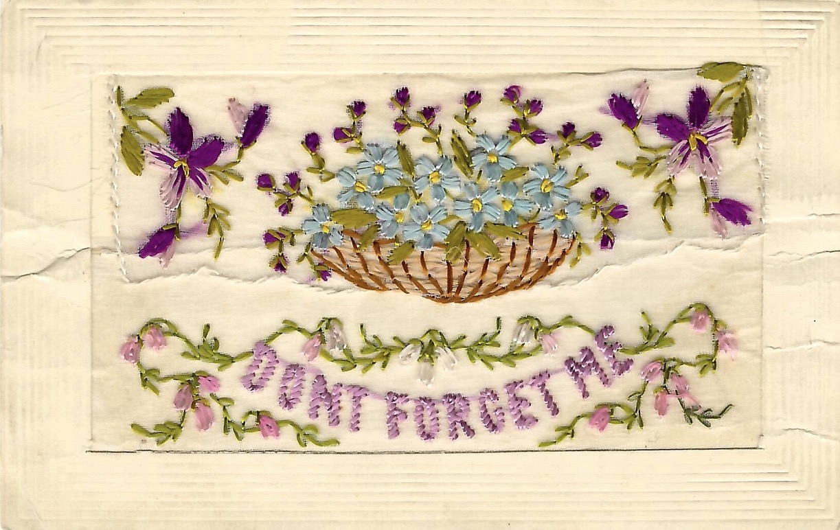 Mail card with fabric embellishment of blue and purple flowers weaved basket, flanked by flowers in the upper right and left corner. Below, vines abloom surround the words “Don’t Forget Me.”