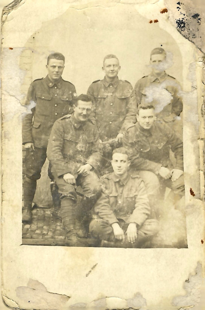 Portrait of six uniformed soldiers kneeling, sitting or standing on a cobbled passage.