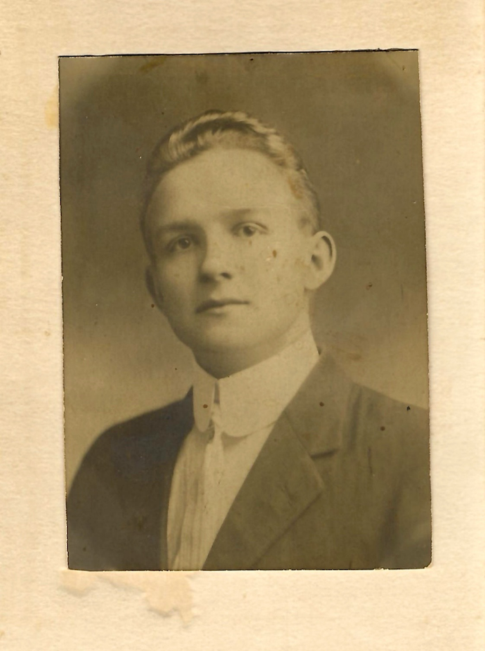 Black-and-white photograph on white background of man dressed in white shirt and tie, donning a dark suit.