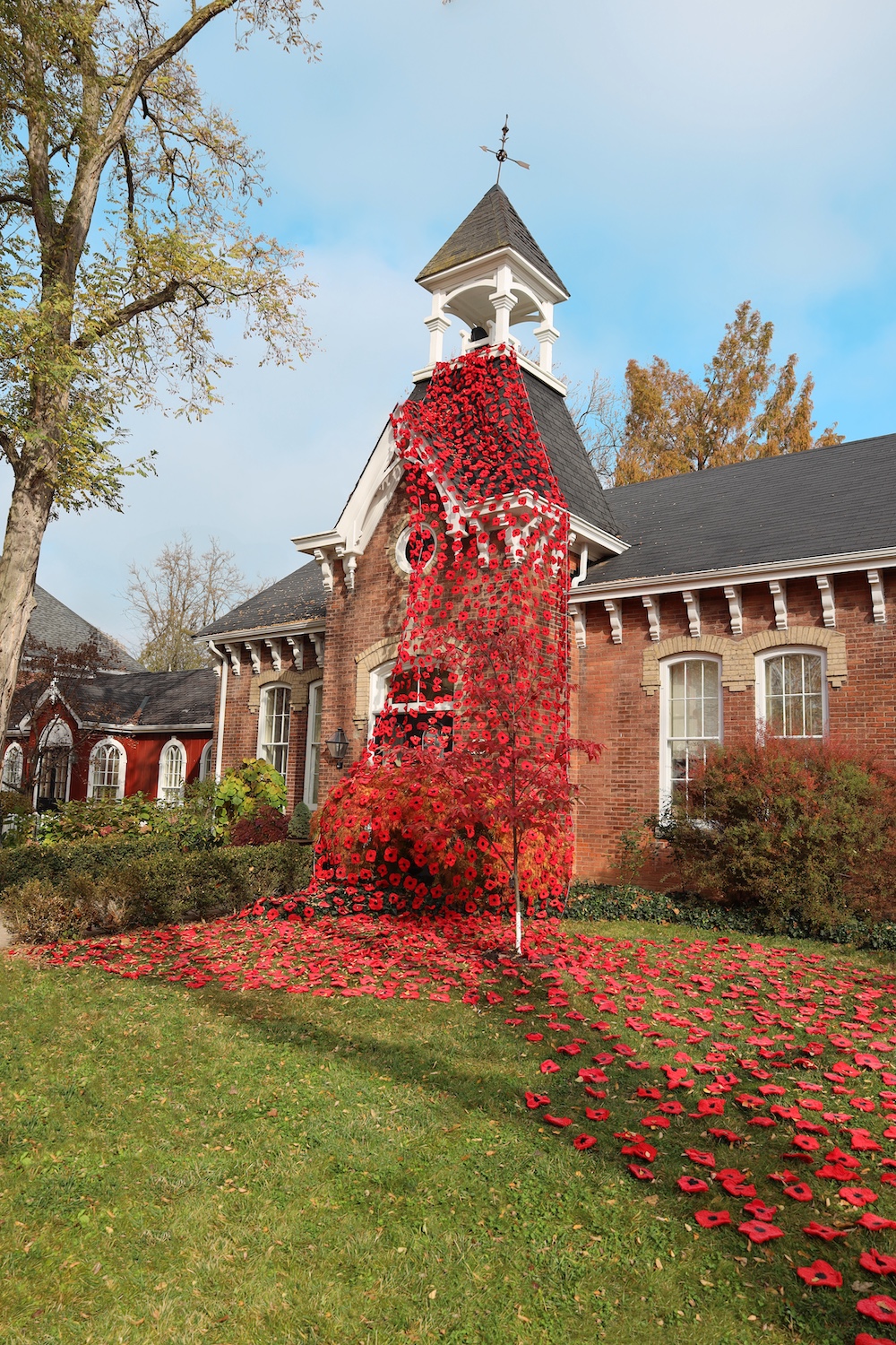 Brick building topped by a bell tower draped with poppies.
